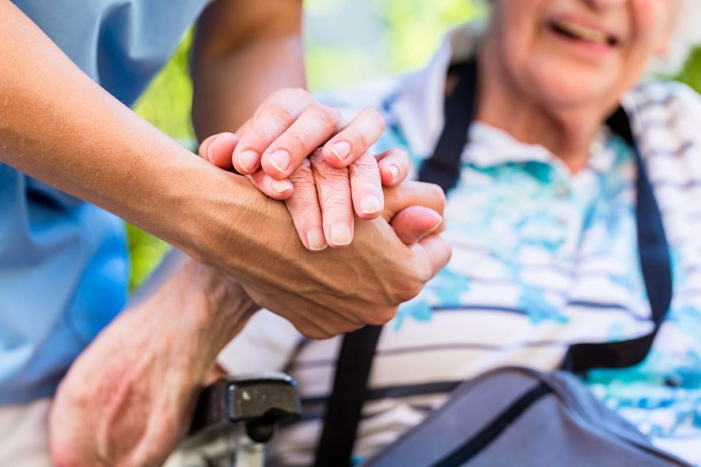 Hands of a nurse and an older adult in assisted living after a stroke