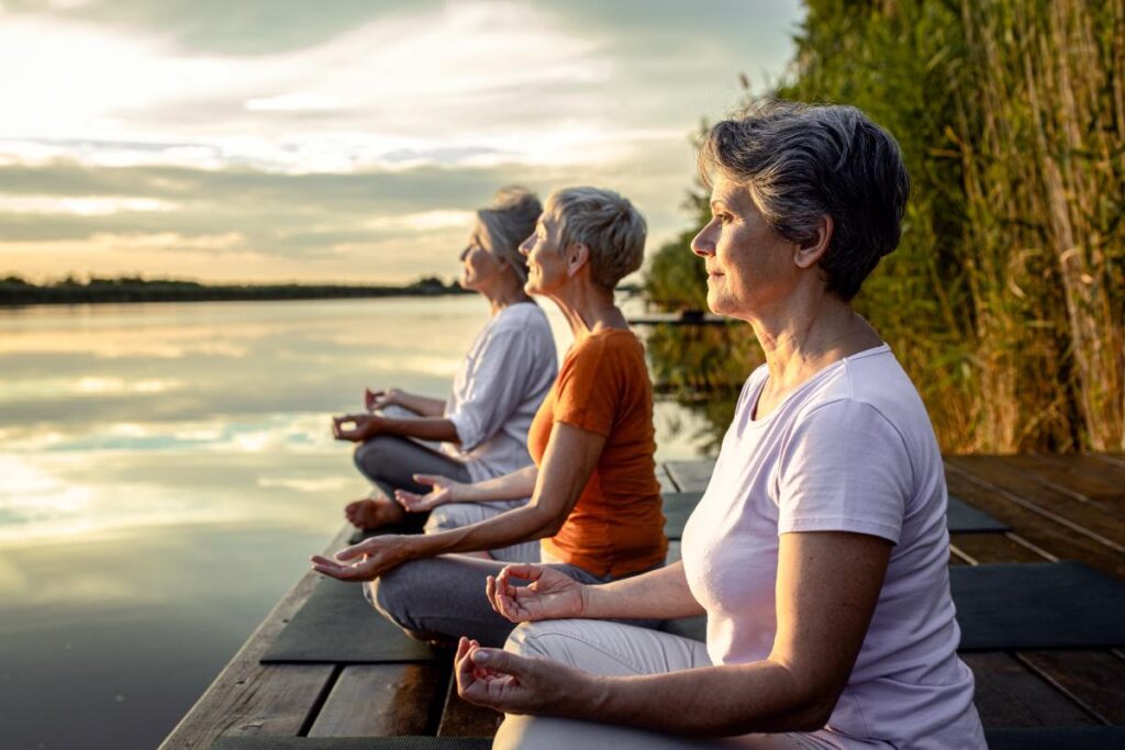 Senior doing yoga by the lake at sunset participating in activities to improve memory