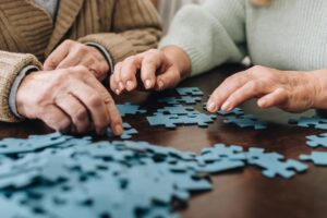 Close-up of two seniors' hands while doing a puzzle and reaping the benefits of puzzles for brain health