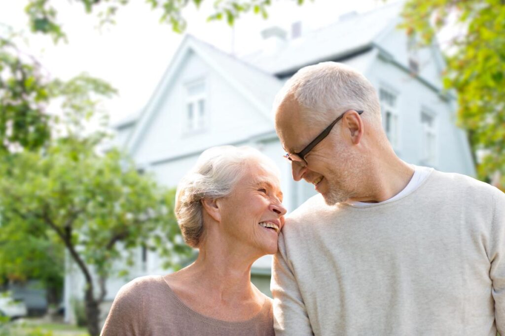 Older couple smiling at each other in front of beautiful property while enjoying the benefits of retiring in texas