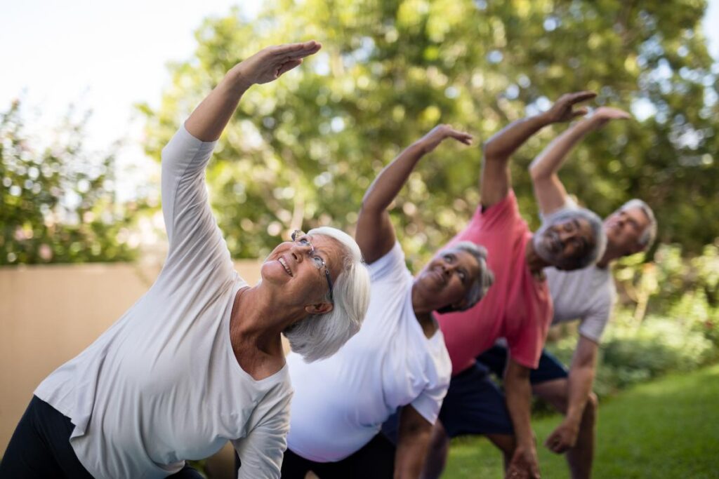 Group of seniors stretching outdoors in the fresh air and sunshine after learning about the importance of physical health in seniors