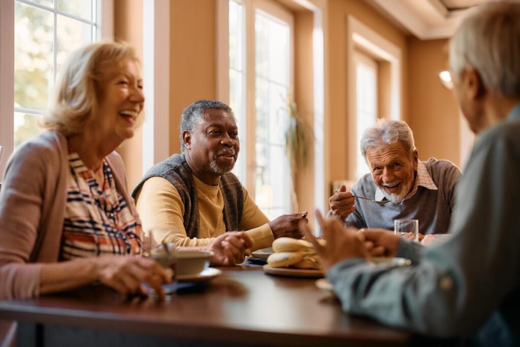 Happy seniors smiling and laughing while enjoying a meal together in an independent living home for seniors