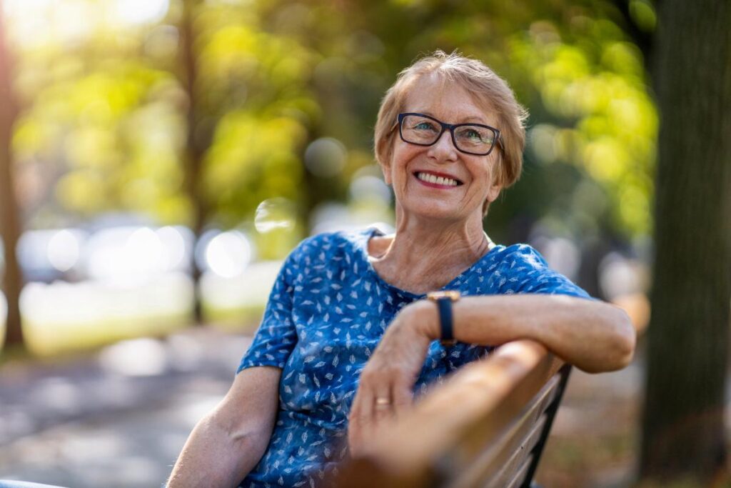 Happy woman smiling while sitting on a park bench and taking a break between participating in outdoor hobbies for seniors in dallas texas