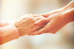 caretaker compassionately grasping the hand of an older adult while providing senior care services