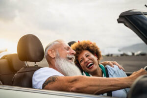 older couple laughing while taking a ride in a sports car while enjoying a luxury senior living lifestyle