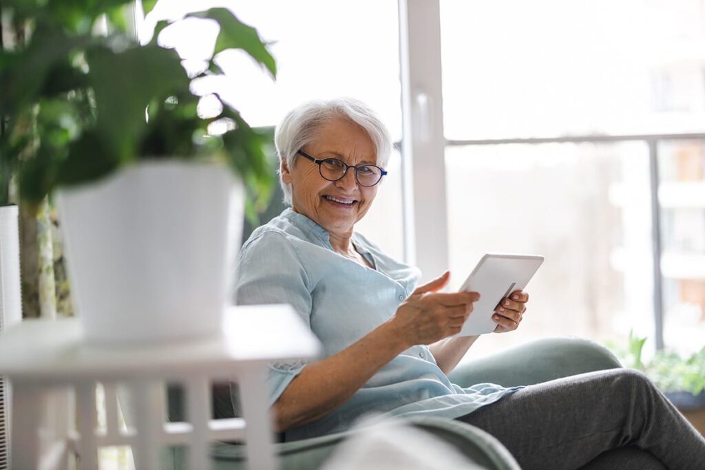 older woman sitting in beautiful sunroom reading answers to the question how much does senior long-term care cost